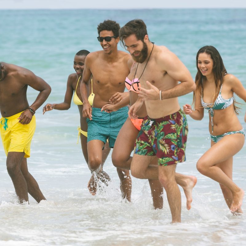Front view of multi ethnic group of friends enjoying and running on sea at beach on sunny day